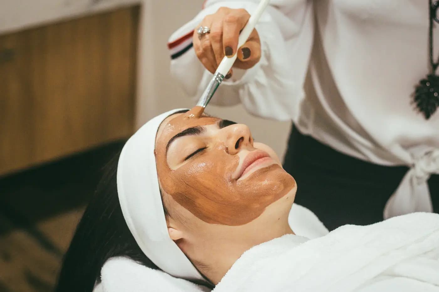 Esteticista a aplicar uma máscara facial com pincel a uma cliente