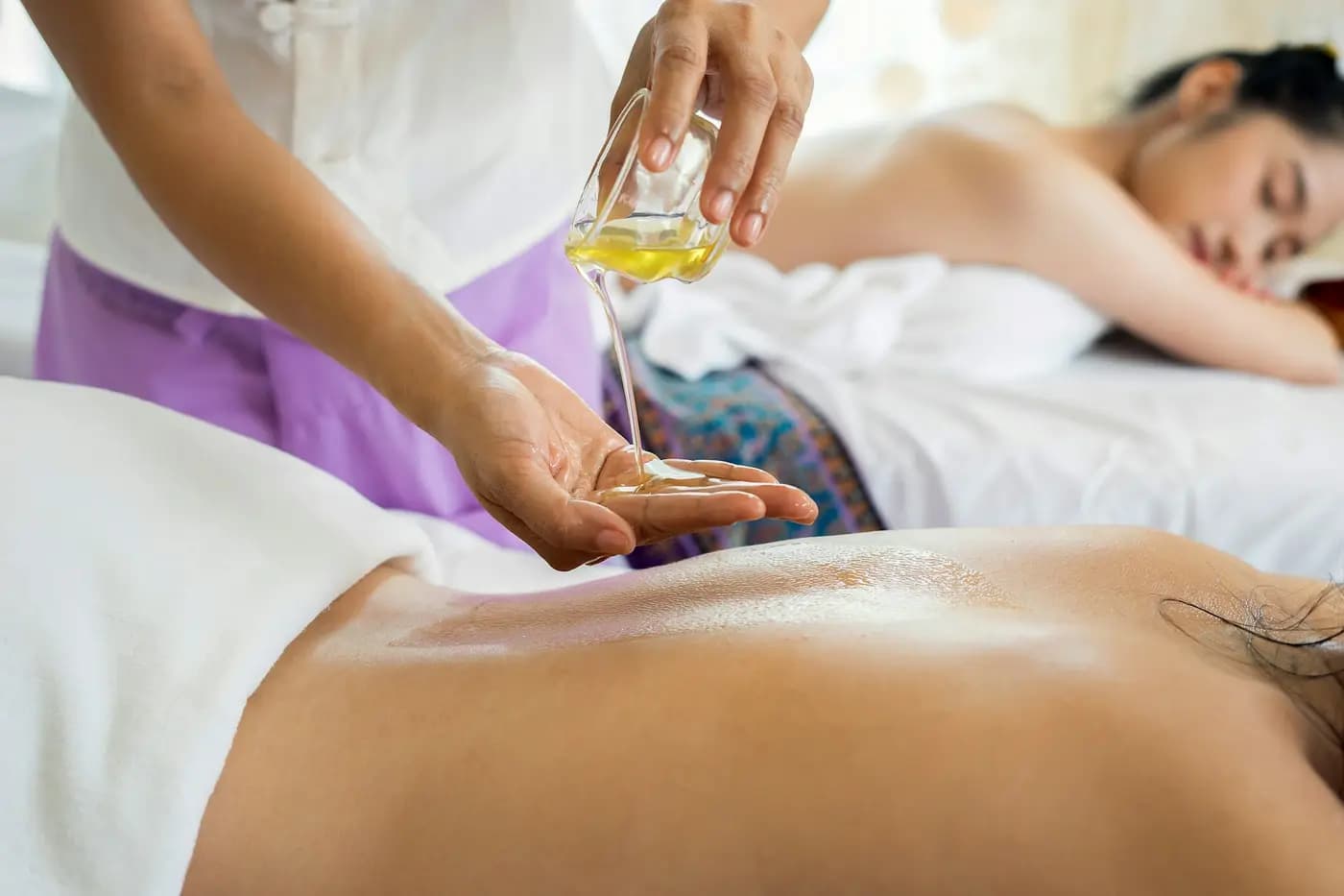 Terapeuta a aplicar óleo nas costas de um cliente numa sala de massagens